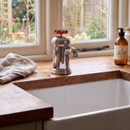 Faucet-shaped mug on a windowsill beside a butler sink